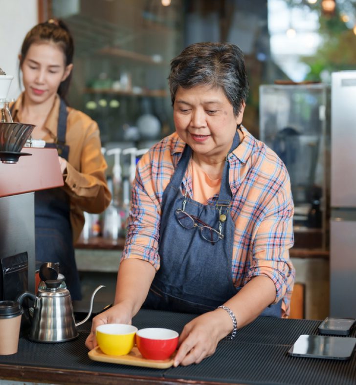 Asian,Senior,Woman,Serving,Coffee,To,Customers,In,Front,Of